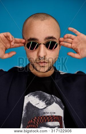 Studio Shot Of A Young Tattoed Bald Man Posing Against A Blue Background. 90s Style.