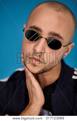 Studio Shot Of A Young Tattoed Bald Man Posing Against A Blue Background. 90s Style.