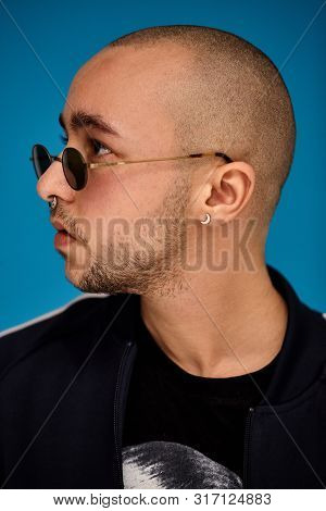 Studio Shot Of A Young Tattoed Bald Man Posing Against A Blue Background. 90s Style.