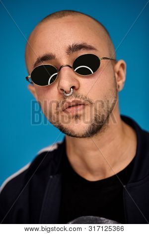 Studio Shot Of A Young Tattoed Bald Man Posing Against A Blue Background. 90s Style.