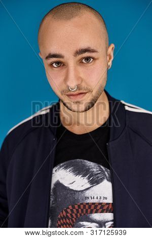 Studio Shot Of A Young Tattoed Bald Man Posing Against A Blue Background. 90s Style.