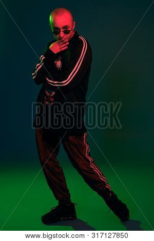 Studio Shot Of A Young Tattoed Bald Man Posing Against A Colorful Background. 90s Style.