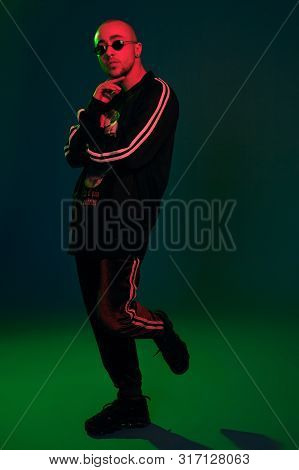 Studio Shot Of A Young Tattoed Bald Man Posing Against A Colorful Background. 90s Style.