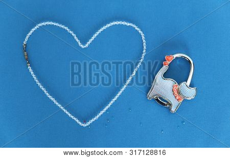 Beads Of Rock Crystal Laid Out In The Shape Of A Heart On A Blue Background. Nearby Is A Lockable Lo