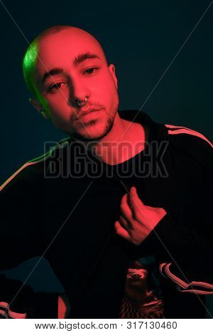 Studio Shot Of A Young Tattoed Bald Man Posing Against A Colorful Background. 90s Style.