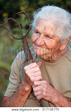 A Closeup Portrait Of An Old Woman With Gray Hair Smiling And Looking Up, Resting Her Chin On A Stic