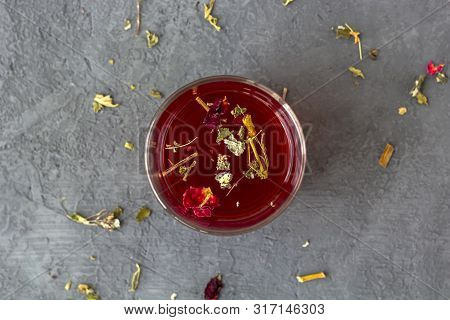 Red Hibiscus Tea In A Glass Cup On A Grey Background Among  With Dry Tea Leaves Hibiscus (karkade, R