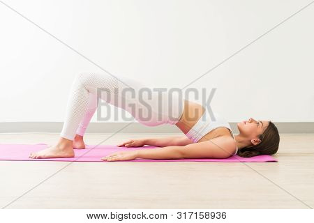 Young Pretty Female Practicing Setu Bandha Sarvangasana While Looking Up In Training Studio
