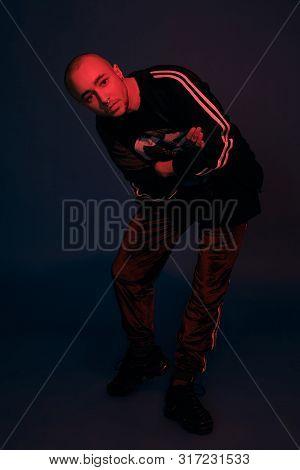 Studio Shot Of A Young Tattoed Bald Man Posing Against A Dark Blue Background. 90s Style.