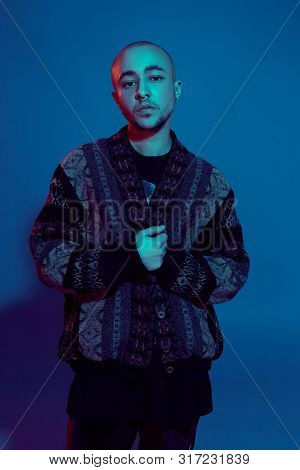 Studio Shot Of A Young Tattoed Bald Man Posing Against A Colorful Background. 90s Style.