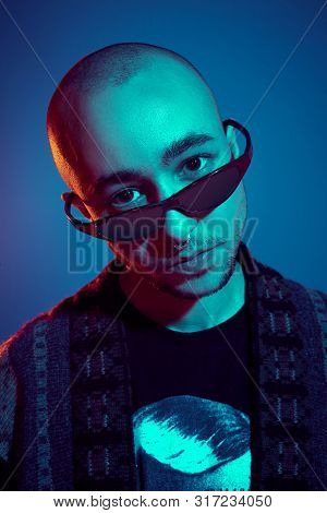 Studio Shot Of A Young Tattoed Bald Man Posing Against A Blue Background. 90s Style.