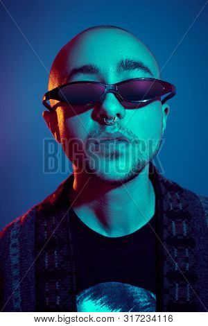 Studio Shot Of A Young Tattoed Bald Man Posing Against A Blue Background. 90s Style.