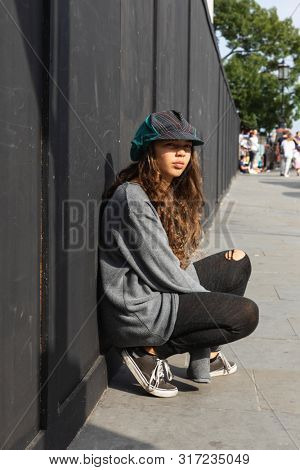 Emotionless girl with colorful hat and long brown hair. Urban context and black background.