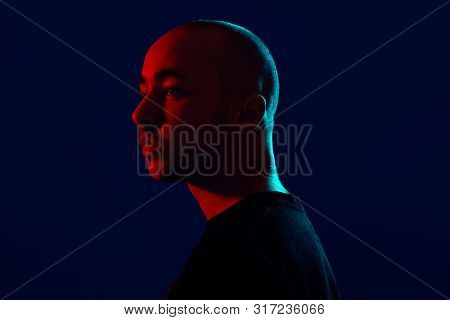 Studio Shot Of A Young Tattoed Bald Man Posing Against A Blue Background. 90s Style.