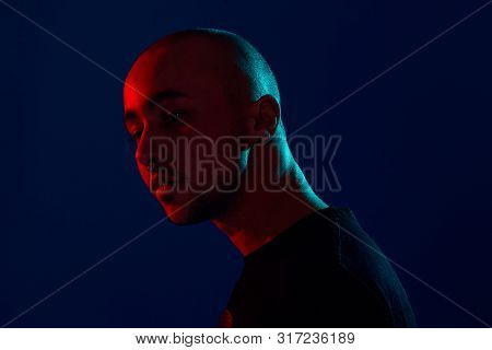 Studio Shot Of A Young Tattoed Bald Man Posing Against A Blue Background. 90s Style.