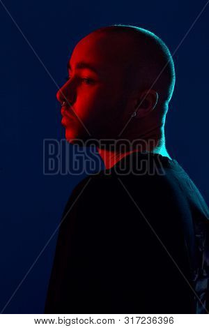 Studio Shot Of A Young Tattoed Bald Man Posing Against A Blue Background. 90s Style.