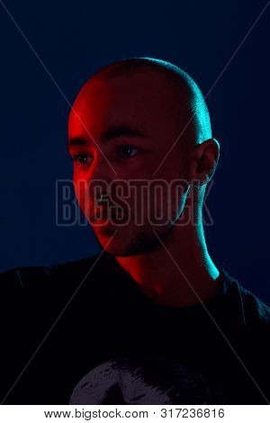 Studio Shot Of A Young Tattoed Bald Man Posing Against A Blue Background. 90s Style.