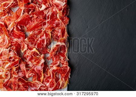 Appetizing Slices Iberian Ham In The Foreground. Olive Oil. Black Background. Space To Insert Your T
