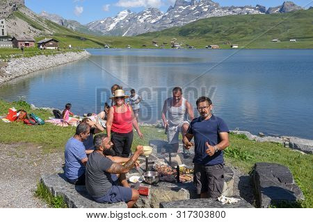 Group Of Happy People Frying Meet On Barbeque Grill At Melchsee-frutt On The Swiss Alps