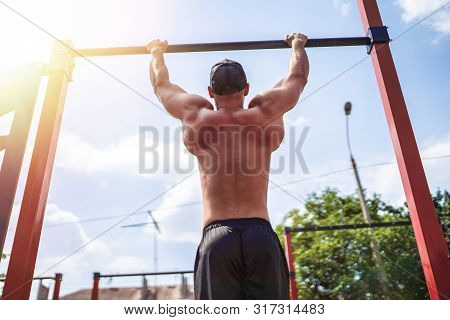 Brutal Athletic Man Making Pull-up Exercises On A Crossbar At Outdoor Streeet Gym. Back View.