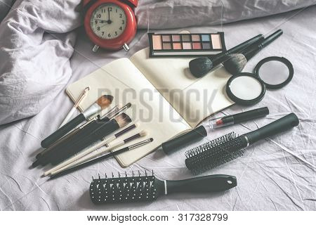 Make Up Cosmetic And Brushes, Alarm Clock And Blank Page Notepad On The Blanket On The Bed Backgroun