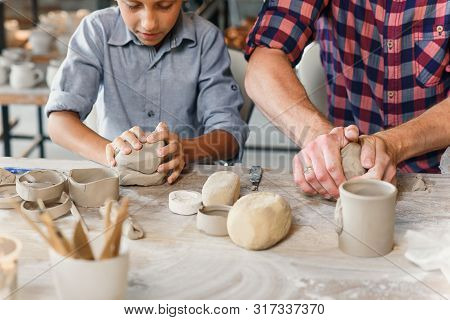 Cute Caucasian Boy Making Part Of Pots While His Father Kneading Clay.