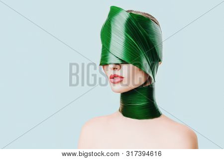 A close up portrait of a beautiful girl with a head rolled up in a leave posing in the studio over the white background. Beauty, nature, make up.
