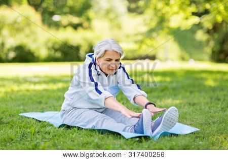fitness, sport and healthy lifestyle concept - happy smiling senior woman exercising on mat at summer park