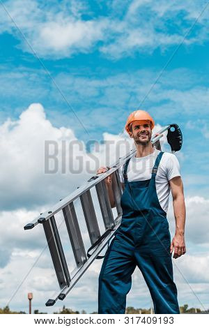 Happy Repairman Holding Ladder And Smiling Against Blue Sky With Clouds