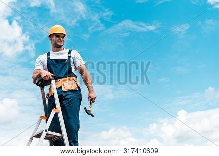 Happy Repairman Standing On Ladder And Smiling Against Blue Sky With Clouds