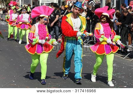 Limassol, Cyprus, March 10th, 2019: Young Man And Two Women In Bright Multi Colored Costumes With Ma