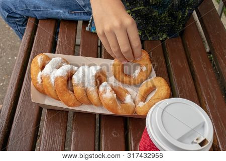 A Teen Boy Sitting On A Bench In Park And Eating Beignet Pastries, Donuts And Drinking Coffee Or Tea