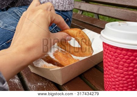 Family Sitting On A Bench In Park And Taking Beignet Pastries, Donuts From A Paper Takeaway Box And 