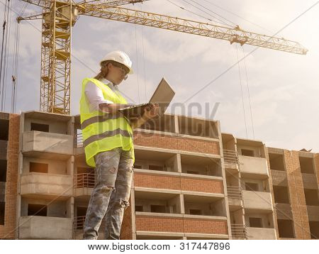 Portrait Of Female Builder Working On Laptop At Construction Site Of High Rise Building. Erection Of