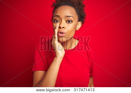 Young beautiful african american woman with afro hair over isolated red background hand on mouth telling secret rumor, whispering malicious talk conversation