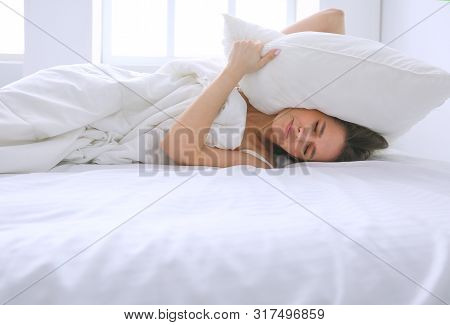 Young Caucasian Woman Covering Her Head And Ears With Pillows.