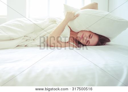 Young Caucasian Woman Covering Her Head And Ears With Pillows.