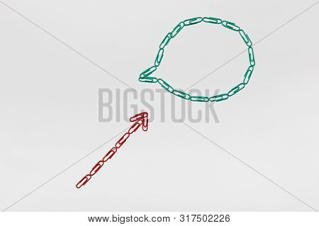 An Arrow Made From Paperclips Pointing Towards A Communication Bubble On White Background, Shot From
