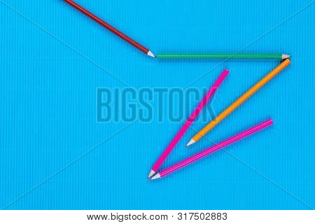 A Bunch Of Crayons Forming An Arrow On An Blue Background, Shot From Above, Closeup.