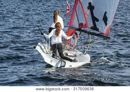 Two Girls Sailing Small Sailboat With Long Red Hair Viewed Closeup From Behind. Teamwork By Junior S