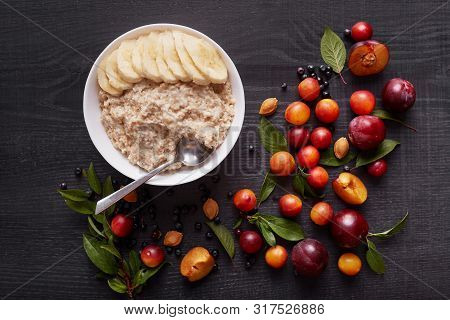 Oatmeal With Banana In White Deep Bowl On Dark Wooden Table. Healthy Breakfast With Oatmeal And Fres