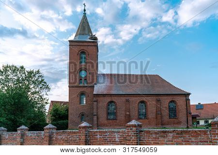 Church In Guelpe, Germany With Two Storks Breeding On The Clock Tower Roof