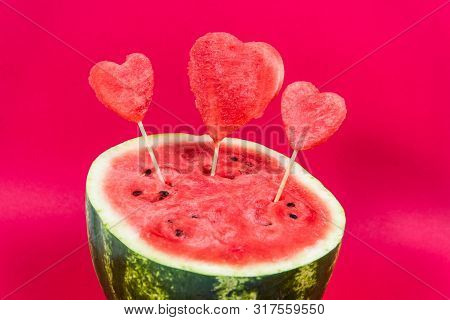 Ripe Juicy Watermelon Decorated With Decorative Hearts On A Wooden Stick, Isolated On A Red Backgrou