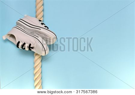 A Pair Of Sports Shoes, The Soles To The Soles Obliquely On A Vertically Hanging Rope. On The Azure 