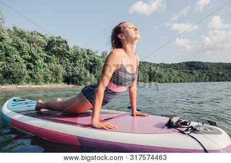 Middle Age Caucasian Woman Practicing Yoga On Paddle Sup Surfboard At Sunset. Female Stretching Doin