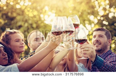 Group Of Happy Friends Drinking And Toasting Wine At Vineyard Before Sunset. Friendship Concept With