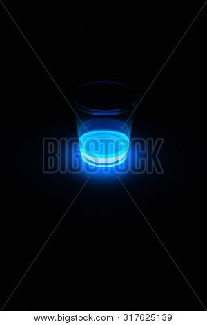 Blue glowing liquid used for glow sticks frequently used for entertainment at parties, concerts, and dance clubs. Glowing in a clear cup. Light emission by Chemiluminescence or chemoluminescence.