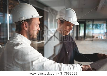 Worker And Engineer Have Meeting While Look Drawing Building Under Constuction. Two Building Enginee