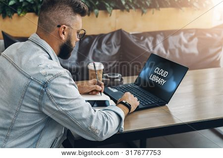 Bearded Man Sitting Indoors, Working On Laptop With Inscription On Monitor- Cloud Library. Guy Reads