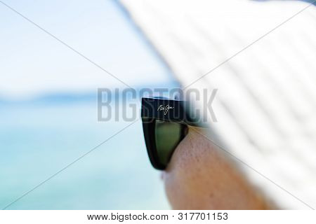 Monaco, France - Aug 15, 2017: Woman With Sun Protection Hat Wearing Maui Jim Sunglasses With Defocu